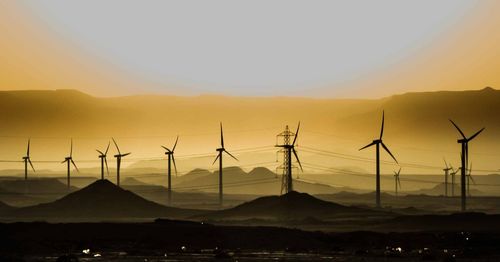 Windmills on landscape against sky during sunset