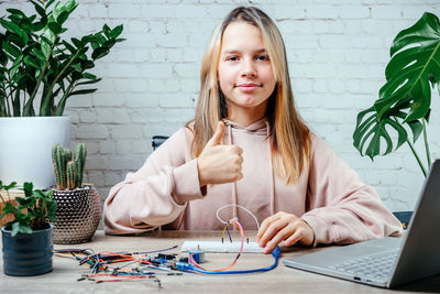 A teenager girl with her thumb up studying robotics at home, stem and arduino coding classes for