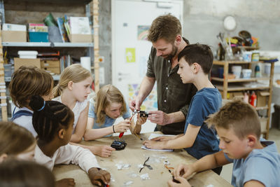 Male teacher helping students while working on robotics project at workshop in school