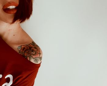 Midsection of woman with tattoo on shoulder against white background