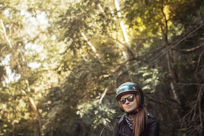 Woman wearing helmet and sunglasses against trees in forest