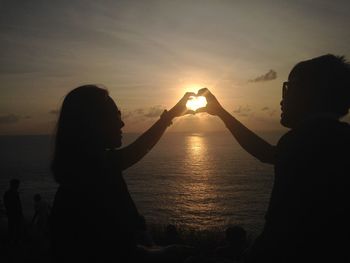 Silhouette people at sea against sky during sunset