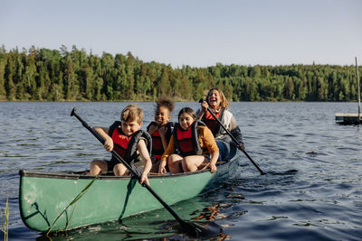 Counselor and kids kayaking on lake against sky at summer camp