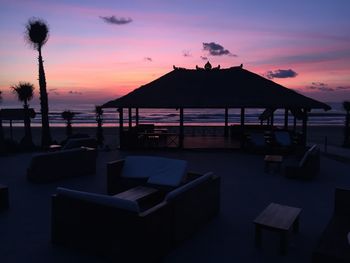 Chairs by swimming pool at beach against sky during sunset