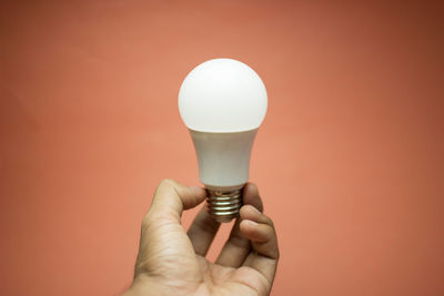 Close-up of hand holding light bulb against wall