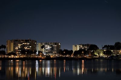 Illuminated buildings by river against sky at night