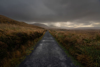 Dark road amidst field against sky