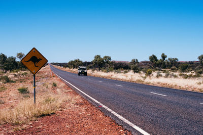 Off-road vehicle moving on road against clear blue sky