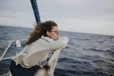 Thoughtful woman looking away while leaning on sailboat