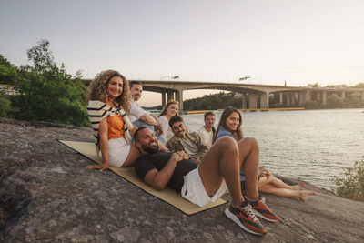 Portrait of smiling male and female friends sitting together on rock during picnic