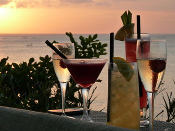 Close-up of drinks on table against sea during sunset