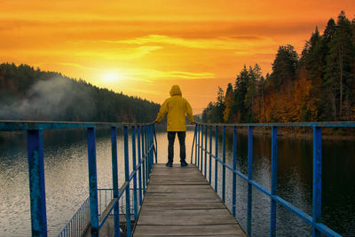 Rear view of man walking on footbridge against sky during sunset