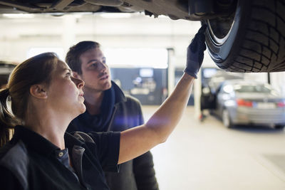 Close-up of mechanic showing wheel to customer under car at repair shop