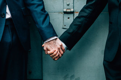 Midsection of homosexual couple holding hands against door during wedding