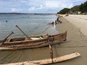 People on boat moored at beach against sky