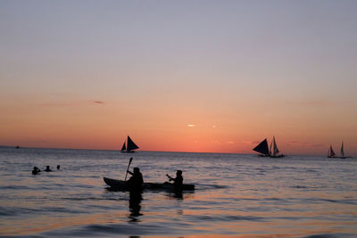 Silhouette people on sea against sky during sunset