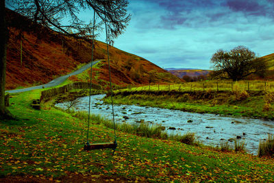 Scenic view of grassy field by lake against sky