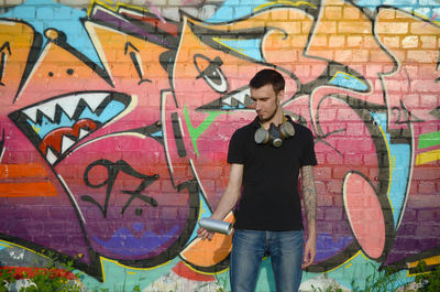 Full length of young man standing against graffiti wall