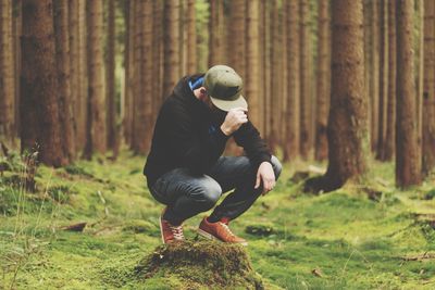 Full length of man wearing cap while crouching in forest