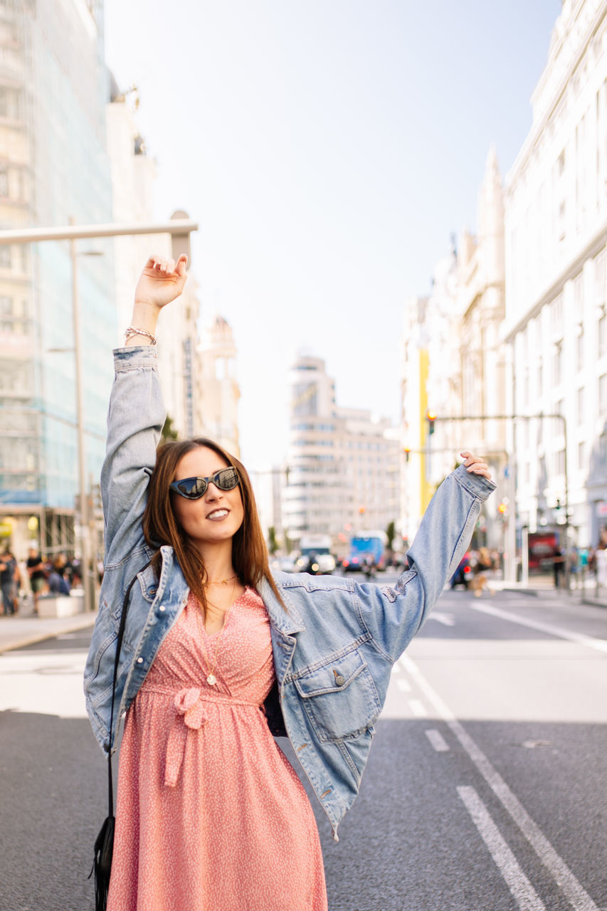 HAPPY WOMAN STANDING ON STREET AGAINST CITY