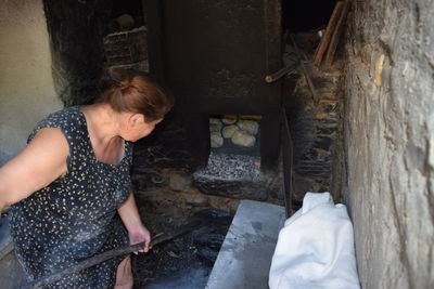 High angle view of woman positioning breads in wood burning stove