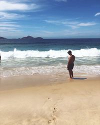 Rear view of man standing on beach against sky