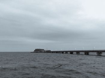 View of suspension bridge over sea against cloudy sky