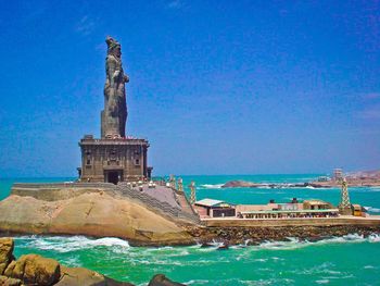 Statue in front of sea against clear blue sky