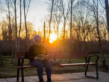 Senior woman reading book in park during sunset