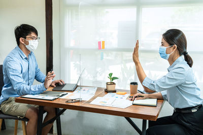 Male and female colleagues talking through shield at office