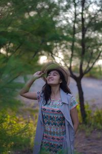 Portrait of smiling young woman standing against trees