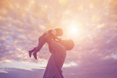 Low angle view of man holding woman against sky during sunset