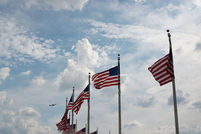 Low angle view of american flags waving against cloudy sky
