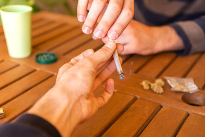 Cropped hands of people sharing cigarette on table