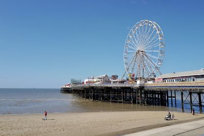 Ferris wheel at beach against clear blue sky