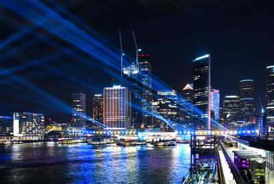 Illuminated city by river against sky at night