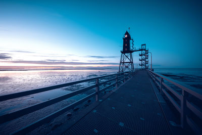 Low angle view of silhouette lighthouse by sea against blue sky during sunset