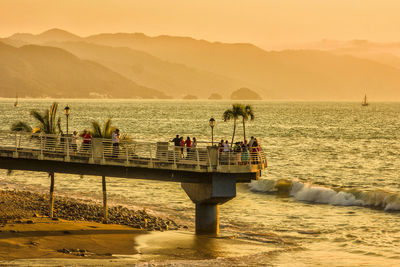 People standing on pier at beach during sunset