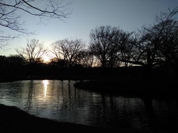 Silhouette bare trees by lake against sky during sunset
