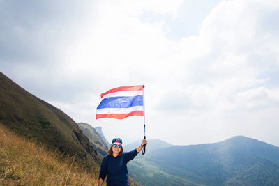 Man with umbrella flag on mountain against sky