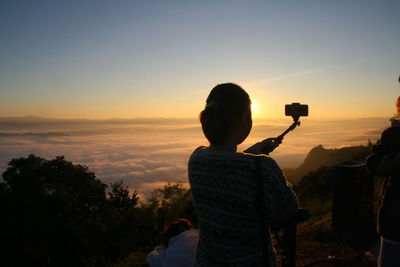 Woman taking selfie while standing on mountain during sunset