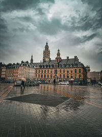 Buildings by river against cloudy sky