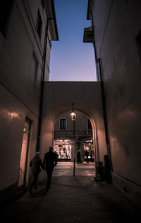 People walking in illuminated building against sky in city