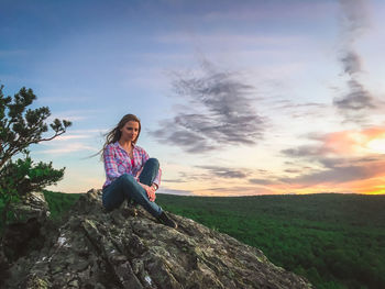 Young woman standing on rock against sky during sunset