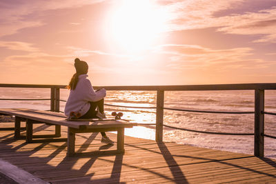 Side view of woman looking at sea while sitting on seat during sunset