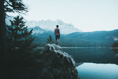 Rear view of man standing on rock by lake