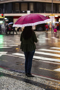 Rear view of woman walking on wet street during monsoon