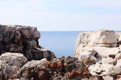 Scenic view of rocks by sea against sky