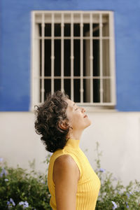Thoughtful woman with eyes closed standing against window