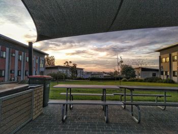 Empty benches by buildings against sky during sunset